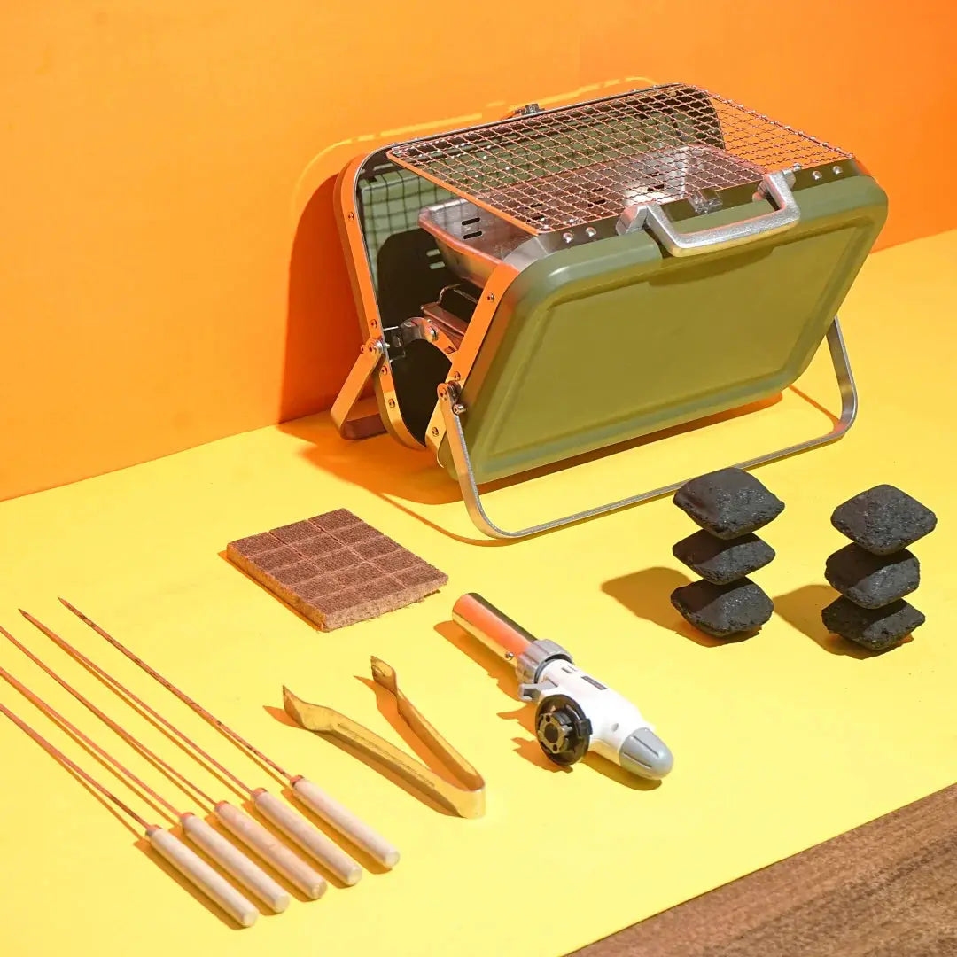 Portable green charcoal grill with metal grate, skewers, tongs, lighter, and charcoal briquettes