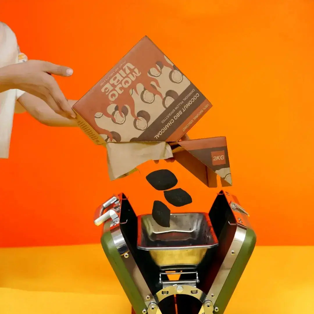 Mojovibe natural coconut BBQ charcoal briquettes from a 2 kg box into a portable green charcoal grill